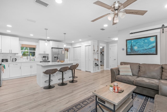 living room featuring a barn door, ceiling fan, sink, and light wood-type flooring