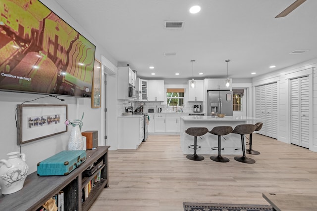 kitchen with tasteful backsplash, stainless steel appliances, pendant lighting, light hardwood / wood-style floors, and white cabinetry