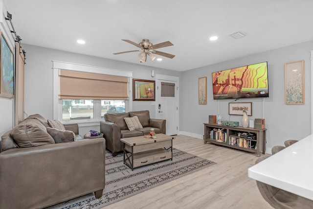 living room featuring a barn door, ceiling fan, and light hardwood / wood-style floors