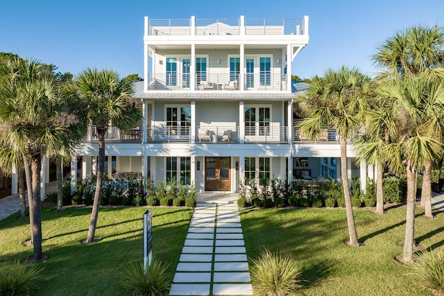 coastal home with french doors, a balcony, and a front lawn