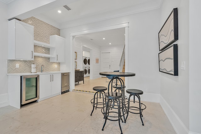 kitchen featuring stacked washing maching and dryer, white cabinetry, ornamental molding, and beverage cooler