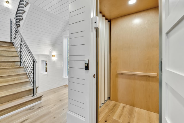 staircase featuring elevator, wood walls, hardwood / wood-style floors, and lofted ceiling