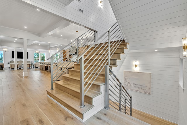 stairway with beam ceiling, wooden ceiling, a notable chandelier, wood-type flooring, and wooden walls