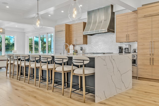 kitchen featuring custom exhaust hood, beam ceiling, a spacious island, and light wood-type flooring