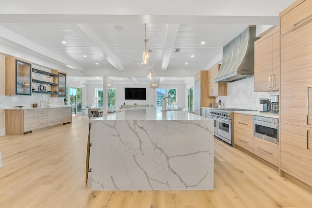 kitchen with beam ceiling, light stone countertops, light hardwood / wood-style floors, and stainless steel appliances