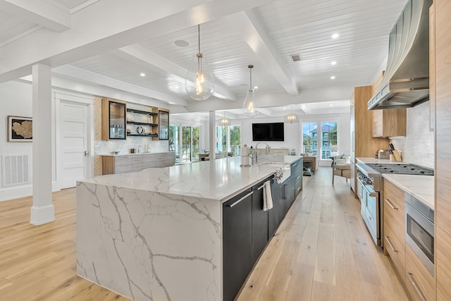 kitchen featuring light stone countertops, a spacious island, wall chimney range hood, light hardwood / wood-style flooring, and hanging light fixtures