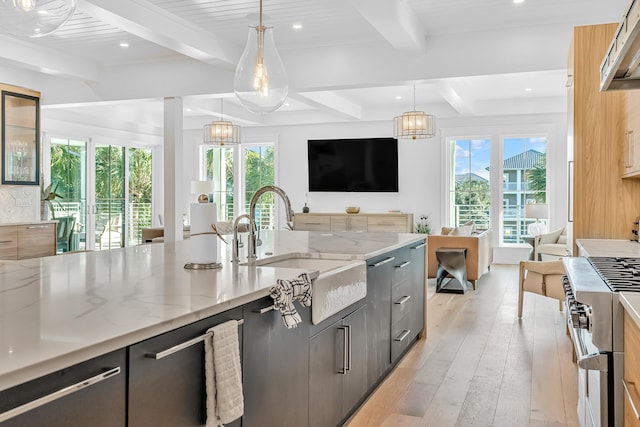 kitchen with light stone counters, light hardwood / wood-style flooring, beamed ceiling, stainless steel stove, and hanging light fixtures