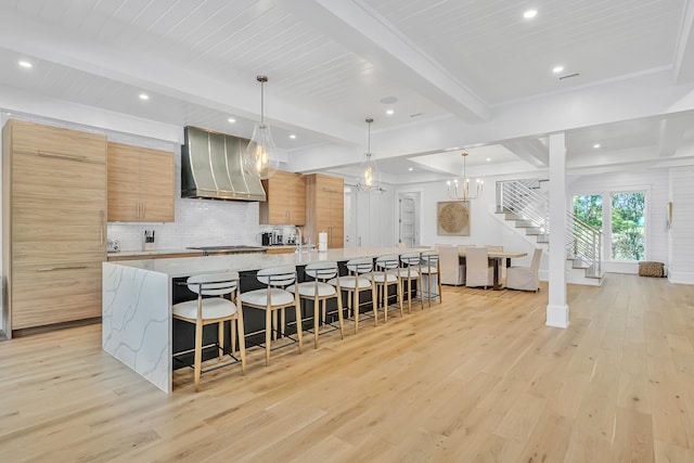 kitchen with custom exhaust hood, a spacious island, light hardwood / wood-style flooring, light stone countertops, and decorative light fixtures