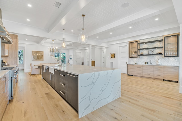 kitchen featuring high end range, light stone counters, a large island with sink, pendant lighting, and light hardwood / wood-style flooring