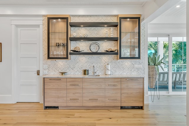 bar with sink, crown molding, decorative backsplash, light hardwood / wood-style floors, and light stone counters