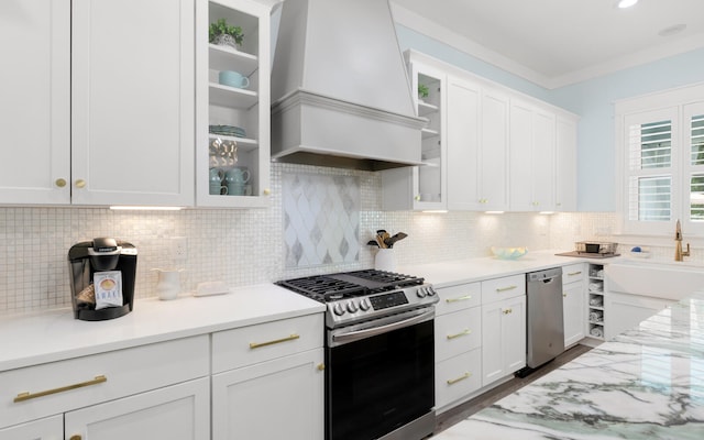 kitchen featuring premium range hood, decorative backsplash, white cabinetry, light stone countertops, and appliances with stainless steel finishes