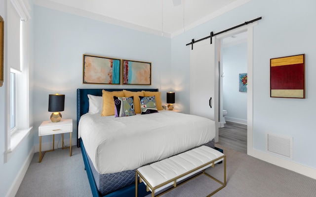 bedroom with ceiling fan, ensuite bathroom, a barn door, and carpet flooring