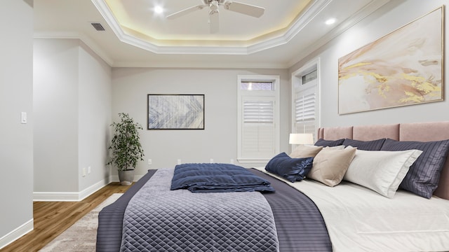 bedroom with a tray ceiling, ceiling fan, crown molding, and hardwood / wood-style flooring