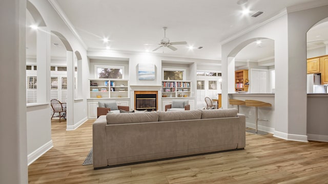 living room with ceiling fan, crown molding, a wealth of natural light, and light hardwood / wood-style flooring