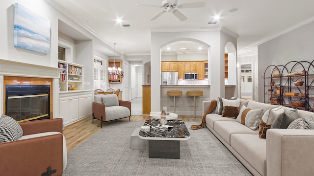 living room with crown molding, a fireplace, ceiling fan with notable chandelier, and light wood-type flooring