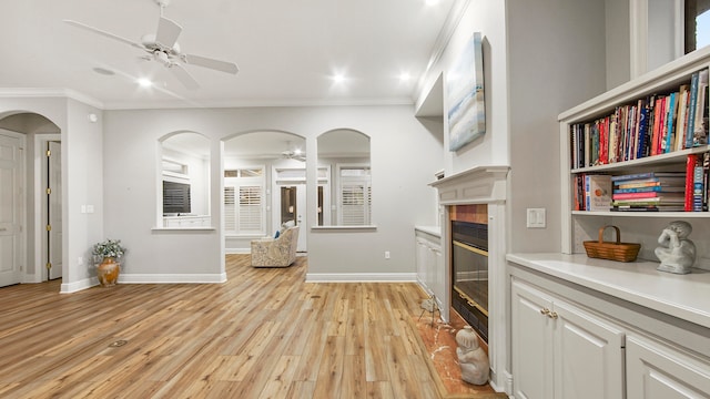 interior space with ceiling fan, crown molding, a tile fireplace, light hardwood / wood-style floors, and white cabinetry