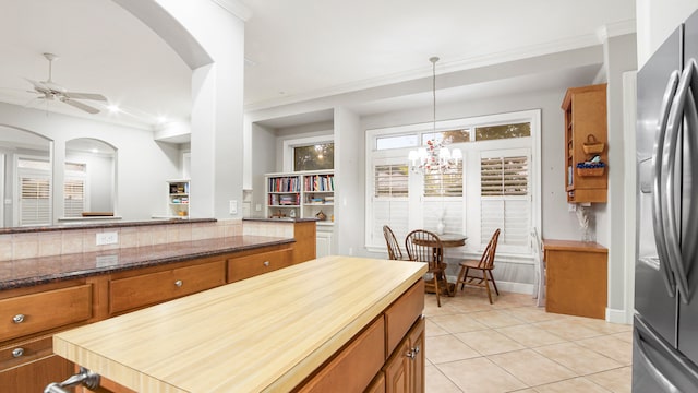 kitchen featuring stainless steel fridge, ceiling fan, light tile patterned floors, dark stone countertops, and hanging light fixtures