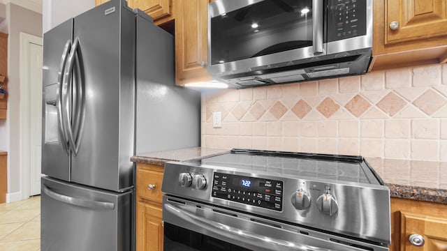 kitchen featuring light tile patterned flooring, stainless steel appliances, dark stone counters, and tasteful backsplash