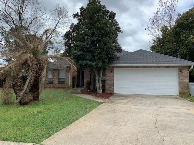 ranch-style home featuring driveway, a shingled roof, a front yard, an attached garage, and brick siding