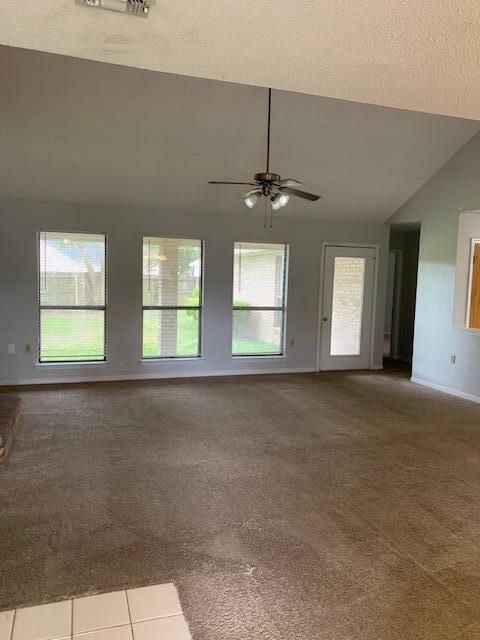 carpeted spare room featuring a ceiling fan, lofted ceiling, a healthy amount of sunlight, and tile patterned flooring