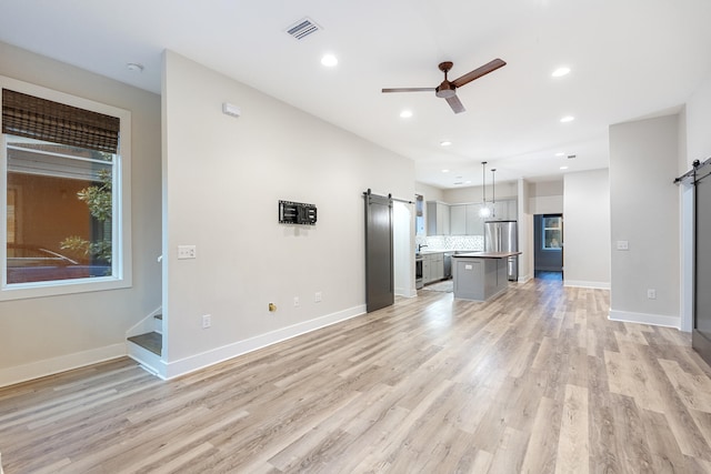 unfurnished living room featuring a barn door, ceiling fan, and light wood-type flooring