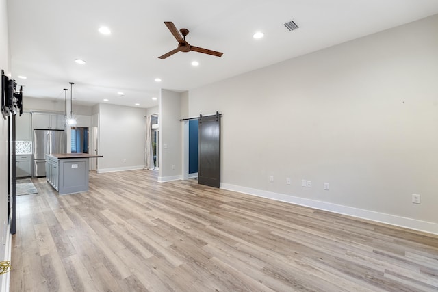 unfurnished living room with a barn door, ceiling fan, and light wood-type flooring