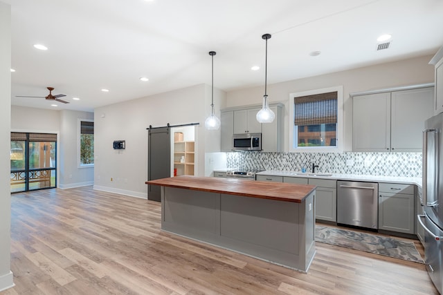 kitchen with butcher block counters, gray cabinets, stainless steel appliances, and a barn door