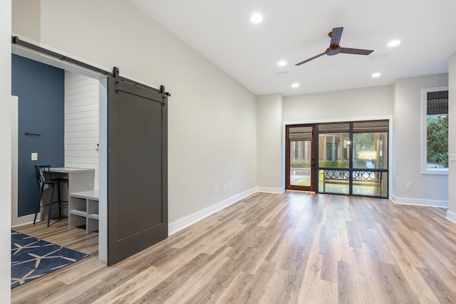 unfurnished living room with ceiling fan, a barn door, and light hardwood / wood-style floors