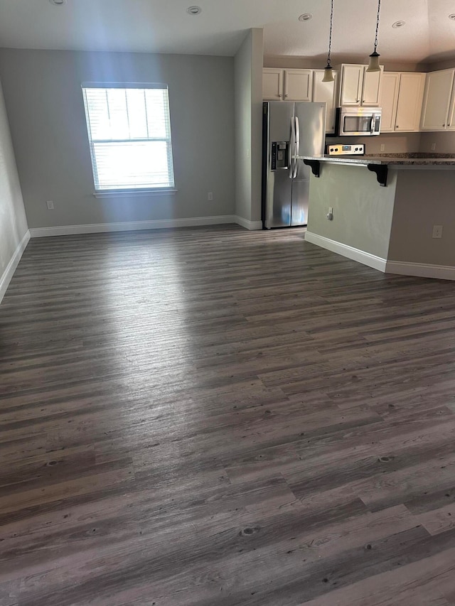 kitchen with dark wood-type flooring, decorative light fixtures, a kitchen bar, white cabinetry, and stainless steel appliances