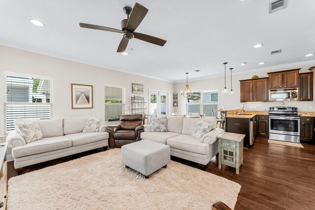 living room with ornamental molding, ceiling fan with notable chandelier, dark hardwood / wood-style floors, and a healthy amount of sunlight