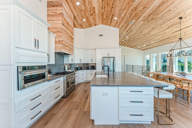 kitchen with a center island with sink, decorative light fixtures, light hardwood / wood-style floors, white cabinetry, and stainless steel appliances