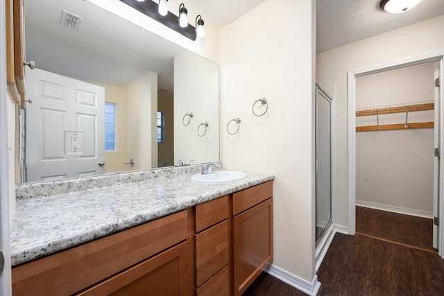 bathroom with a textured ceiling, vanity, hardwood / wood-style flooring, and a shower with door