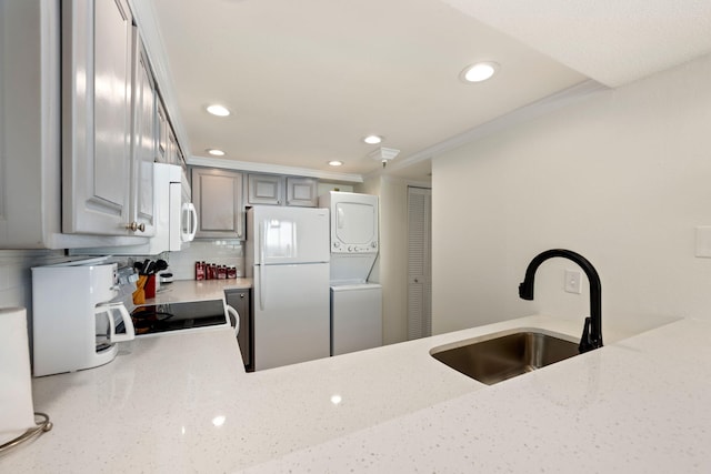 kitchen featuring white appliances, stacked washer / dryer, sink, gray cabinets, and tasteful backsplash