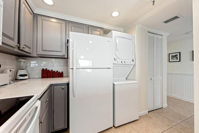 kitchen with white fridge, light tile patterned flooring, gray cabinetry, crown molding, and stacked washing maching and dryer