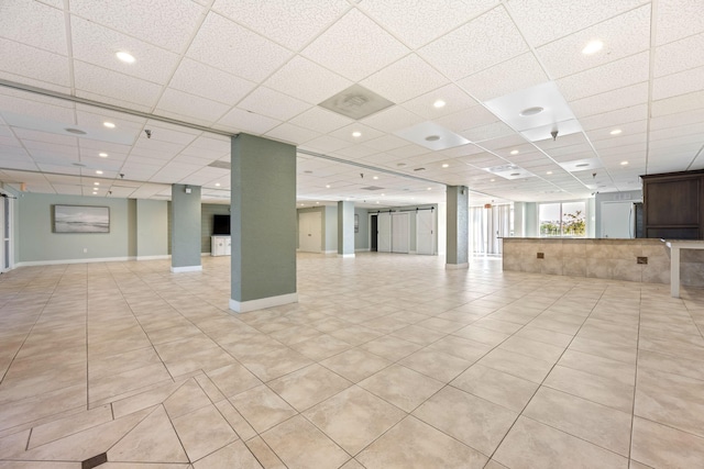 unfurnished living room with a barn door, light tile patterned floors, and a paneled ceiling