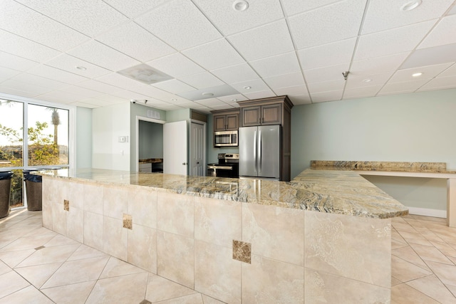 kitchen with appliances with stainless steel finishes, light tile patterned flooring, light stone countertops, and kitchen peninsula