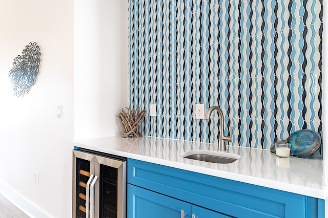 bar featuring blue cabinets, beverage cooler, and sink