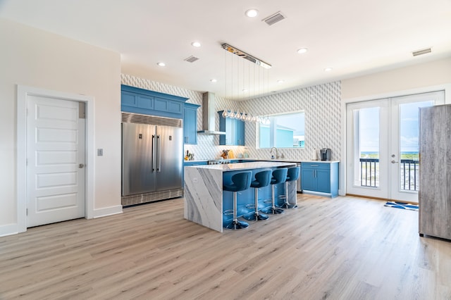 kitchen featuring wall chimney exhaust hood, a breakfast bar, light hardwood / wood-style flooring, a center island, and built in refrigerator