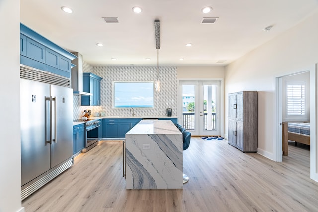 kitchen with wall chimney exhaust hood, light hardwood / wood-style floors, appliances with stainless steel finishes, and french doors