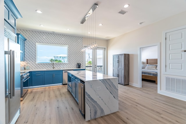 kitchen with light stone countertops, a center island, pendant lighting, light hardwood / wood-style floors, and high end appliances