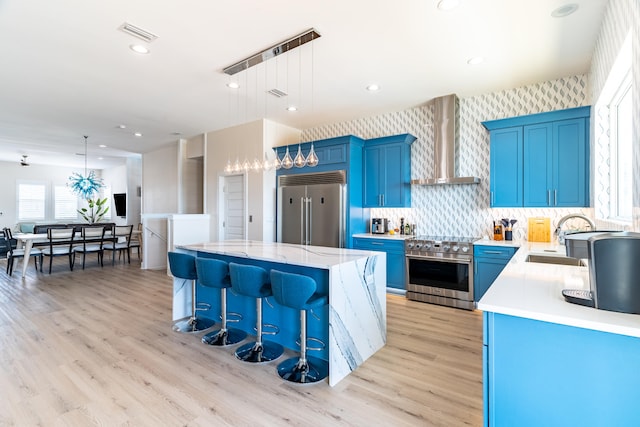 kitchen featuring wall chimney exhaust hood, sink, high quality appliances, a kitchen island, and hanging light fixtures