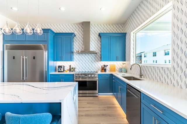 kitchen with sink, wall chimney exhaust hood, hanging light fixtures, decorative backsplash, and appliances with stainless steel finishes