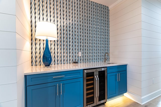 bar with blue cabinets, light hardwood / wood-style flooring, beverage cooler, and sink