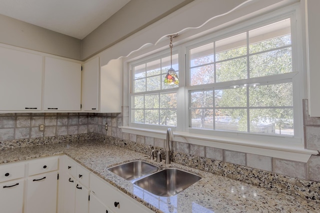 kitchen with light stone countertops, backsplash, white cabinetry, and sink