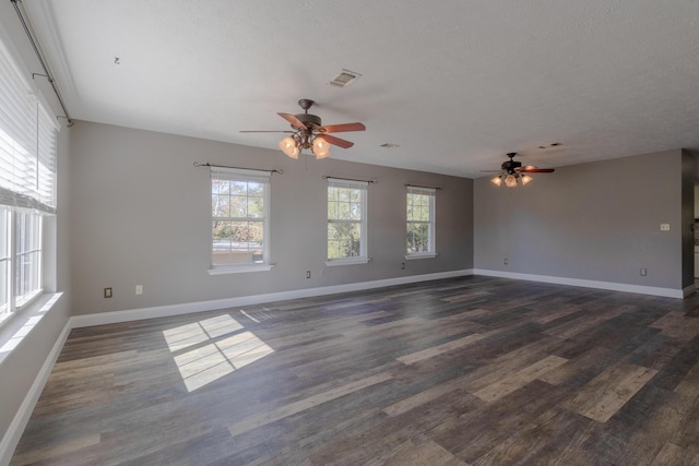 spare room with a textured ceiling, ceiling fan, dark wood-type flooring, and a wealth of natural light