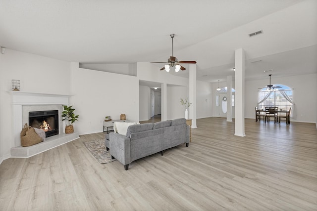 living room featuring a tiled fireplace, ceiling fan, light hardwood / wood-style flooring, and vaulted ceiling