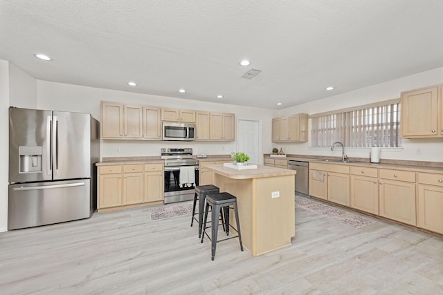 kitchen with a center island, sink, light wood-type flooring, appliances with stainless steel finishes, and a kitchen bar