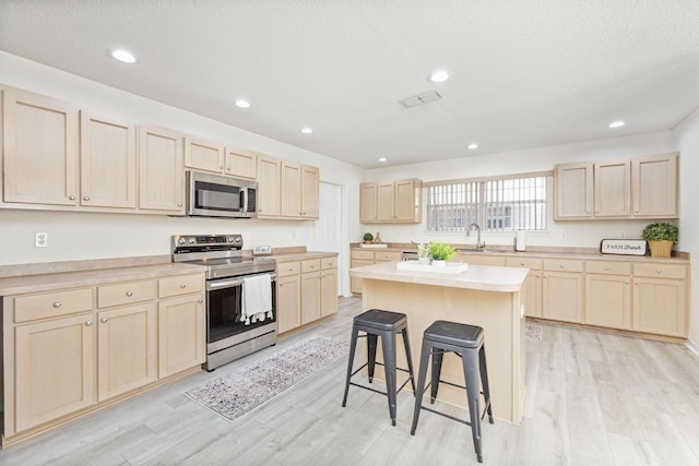 kitchen with a center island, stainless steel appliances, light hardwood / wood-style floors, a textured ceiling, and a breakfast bar