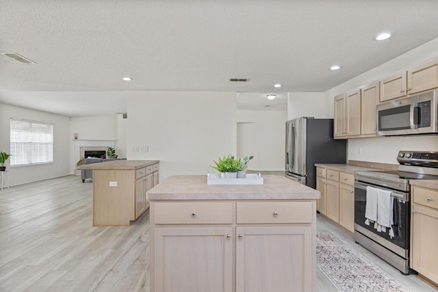 kitchen featuring a center island, light brown cabinets, stainless steel appliances, a textured ceiling, and light wood-type flooring