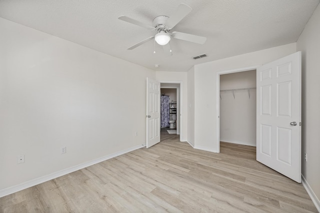 unfurnished bedroom with a walk in closet, a textured ceiling, ceiling fan, light hardwood / wood-style flooring, and a closet